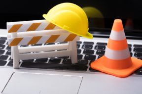 Road,Barrier,With,Hard,Hat,And,Traffic,Cone,On,Laptop