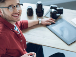 Happy freelancer man sitting by working table with graphic tablet